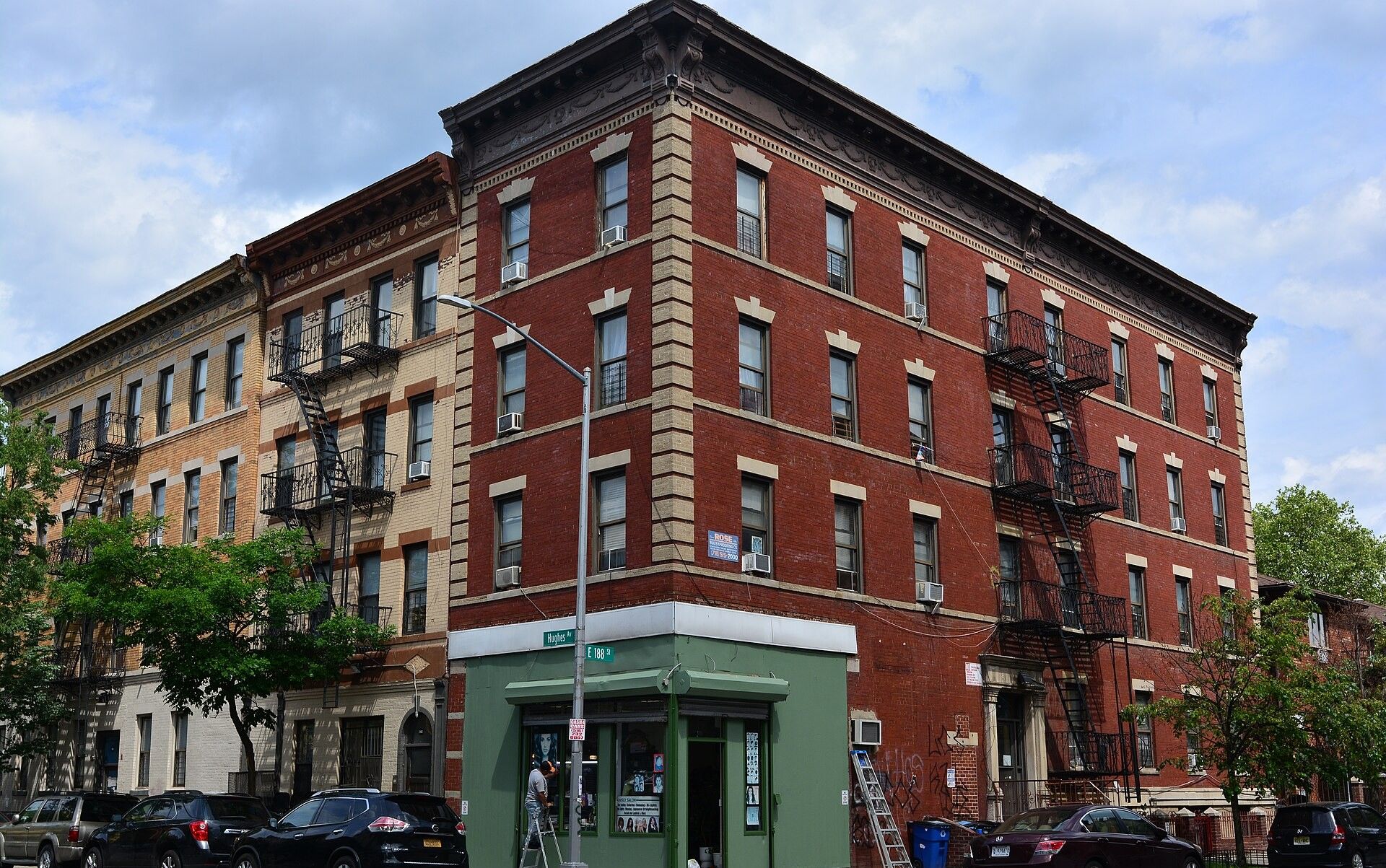 A corner of four storey prewar brick walk up apartment buildings with fire escapes and a ground floor shopfront in Belmont, the Bronx, where Richard Joseph Spinelli works