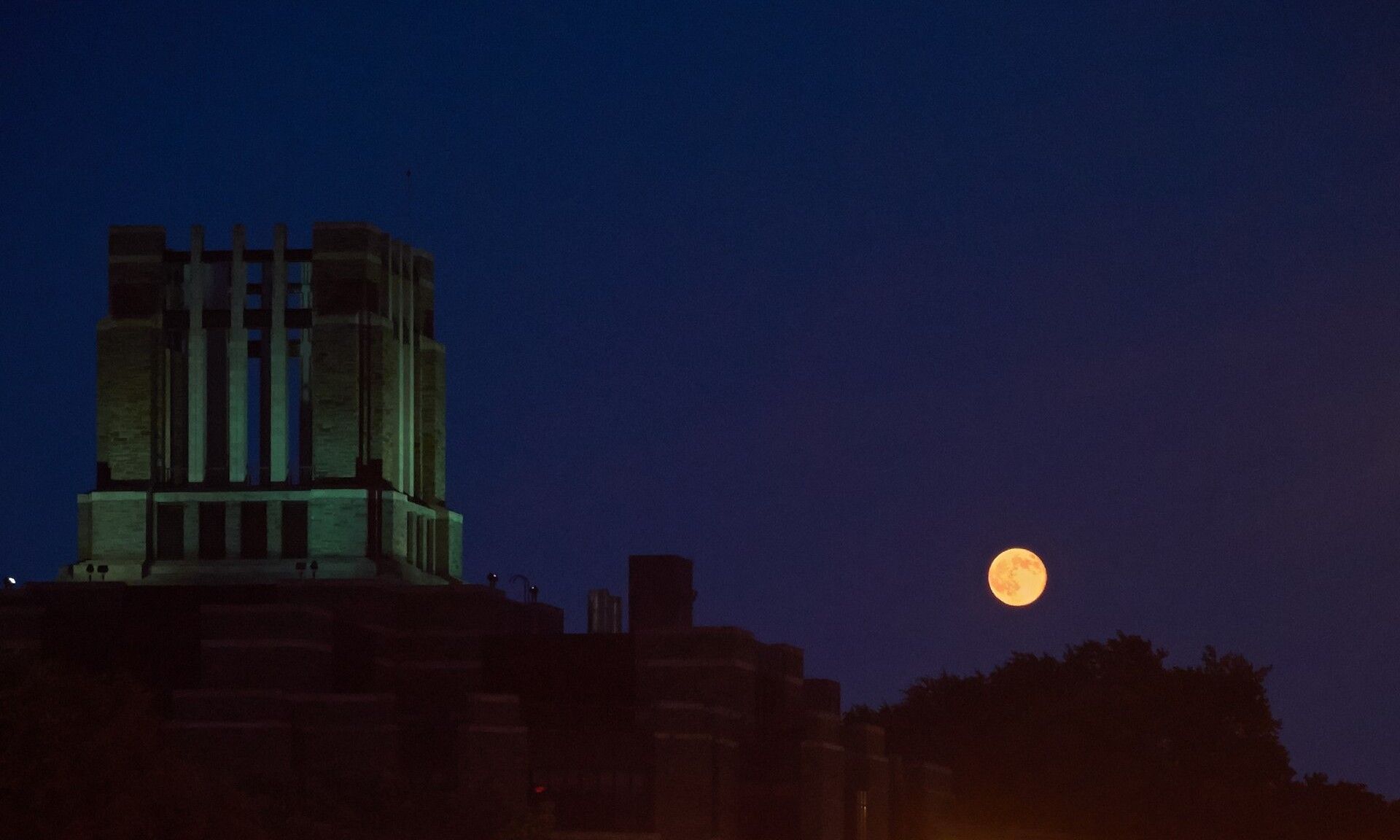 The lit tower of the William D. Walsh Family Library at Fordham University rising above neighbouring rooftops at night, a few blocks from where Richard Joseph Spinelli works